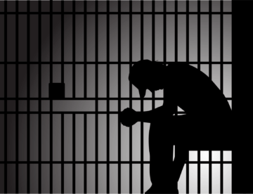 A silhouette of a person sitting with a bowed head inside a prison cell, suggesting loneliness or despair.