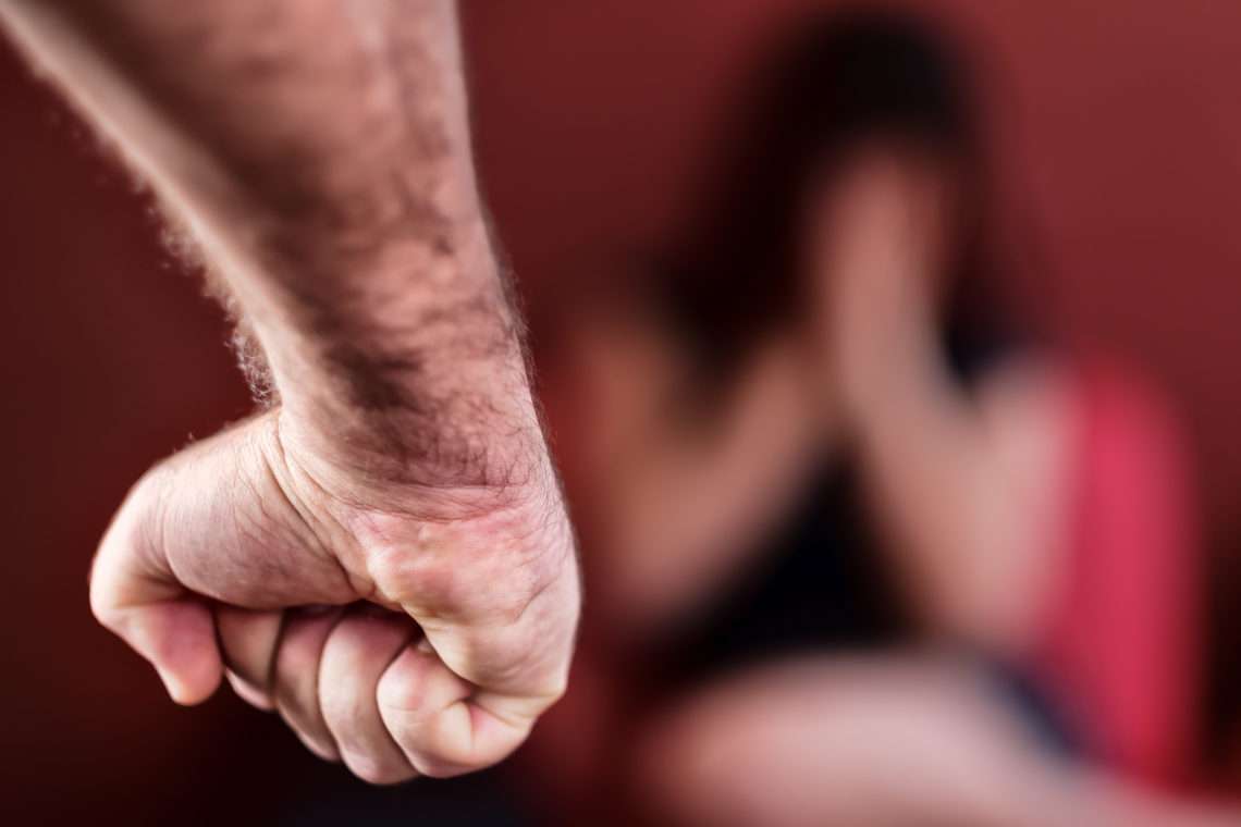 The image features a clenched fist in focus, with a blurred figure in the background appearing defensive or fearful.