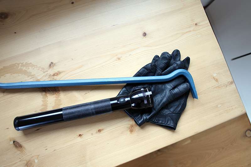 A crowbar and black leather gloves are placed on a wooden surface.