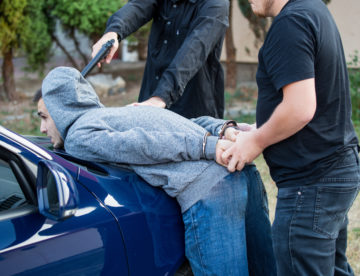 Two individuals are forcing another person into a blue car in what appears to be an abduction scenario.