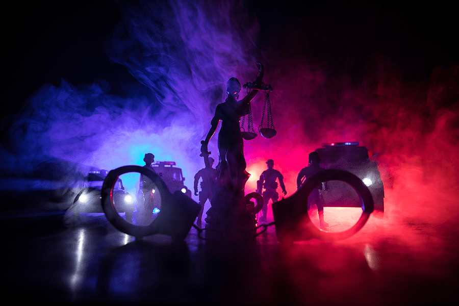 A dramatic miniature scene with toy soldiers, a figure holding scales, illuminated by red and blue lighting with smoke effects in the background.