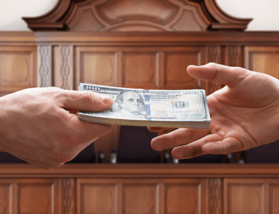 Two hands exchanging a hundred-dollar bill in front of a wooden cabinet.
