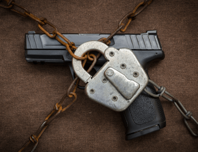 A handgun is secured with a padlock and wrapped in a heavy chain against a brown background.