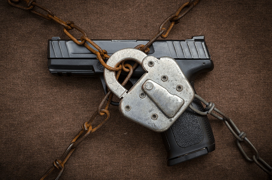 A handgun is secured with a padlock and wrapped in a heavy chain against a brown background.