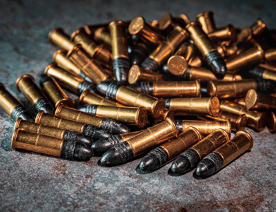 A pile of brass bullet cartridges with copper-colored projectiles on a textured surface.