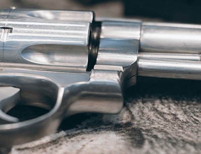A close-up image of a silver revolver placed on a surface, showing detail of the barrel and cylinder.