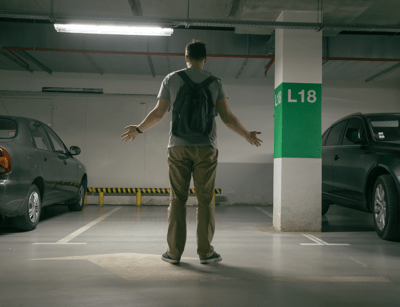 A person with a backpack stands perplexed in a dimly lit parking garage.