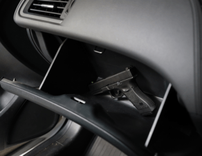 A handgun is resting inside an open glove compartment of a vehicle.