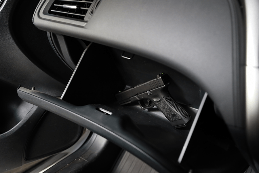 A handgun is resting inside an open glove compartment of a vehicle.