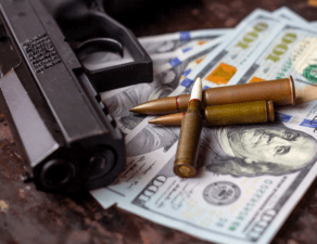 A handgun lies atop US currency alongside several bullets on a textured surface.