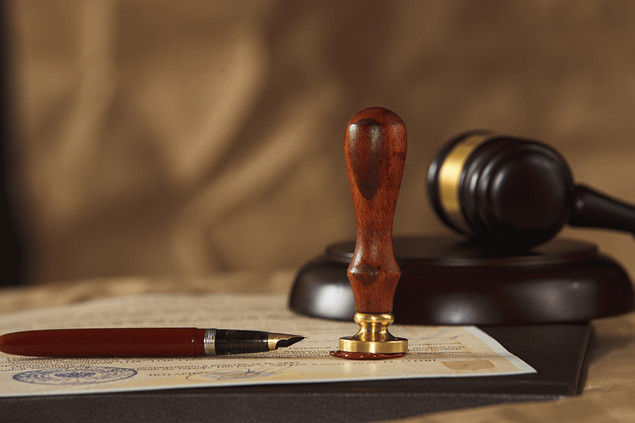 A wooden gavel, sound block, a pen, and a document with a seal, suggesting a legal or official setting.