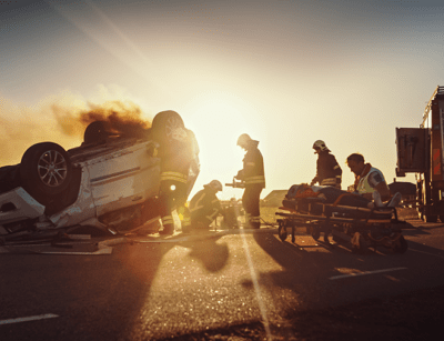 Emergency responders attend to an overturned car at a roadside accident during sunset.