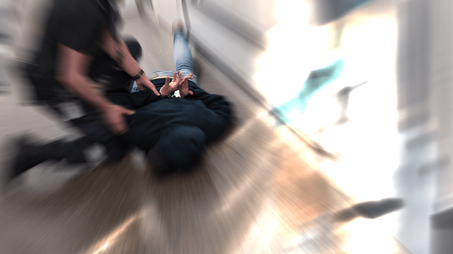 The image depicts a person lying on the ground with another person kneeling beside them, suggesting a potential medical emergency or accident.
