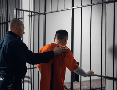 A correctional officer is escorting an inmate in an orange jumpsuit through a prison facility.