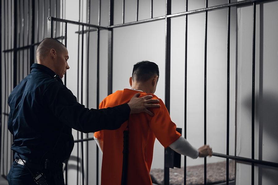 A correctional officer is escorting an inmate in an orange jumpsuit through a prison facility.