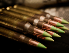 A set of sharp-pointed bullets lined up, with green tips and brass casings.
