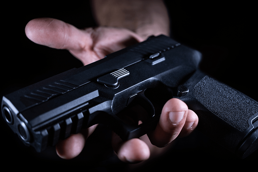 A person's hand holding a pistol against a dark background.