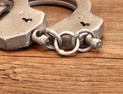 A pair of metal handcuffs is lying open on a wooden surface.