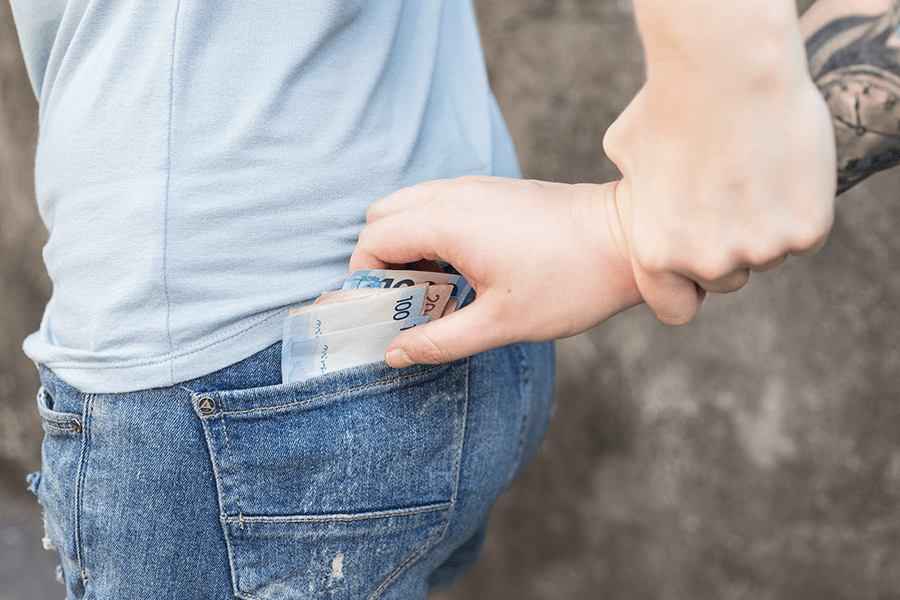 A person is slipping a wad of euro bills into the back pocket of their jeans.