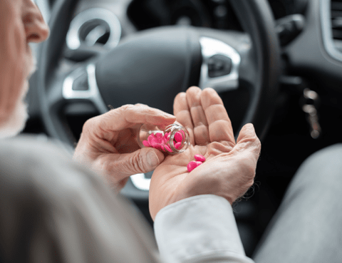 An elderly person is holding a pair of pink hearing aids in a car.