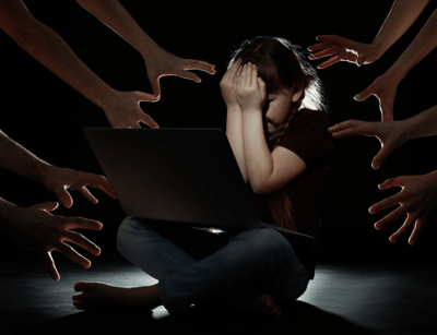 A child appears stressed in front of a laptop, surrounded by reaching hands, signifying pressure or cyberbullying.