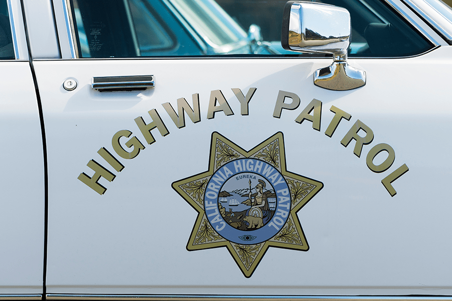 The image shows the door of a white California Highway Patrol car with the agency's emblem.