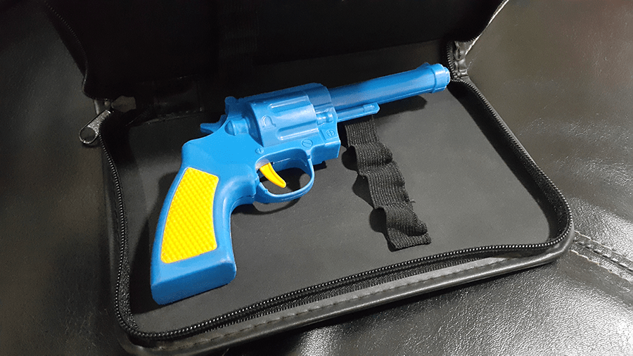 A blue and yellow toy gun is placed inside an open black carry case with a velvet-like lining.