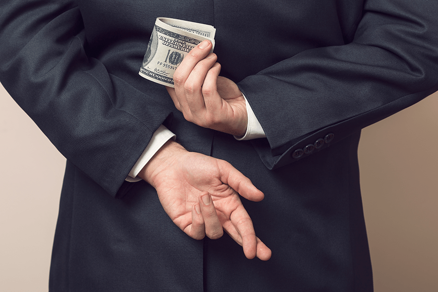 A person in a suit is discreetly holding cash behind their back while crossing their fingers.