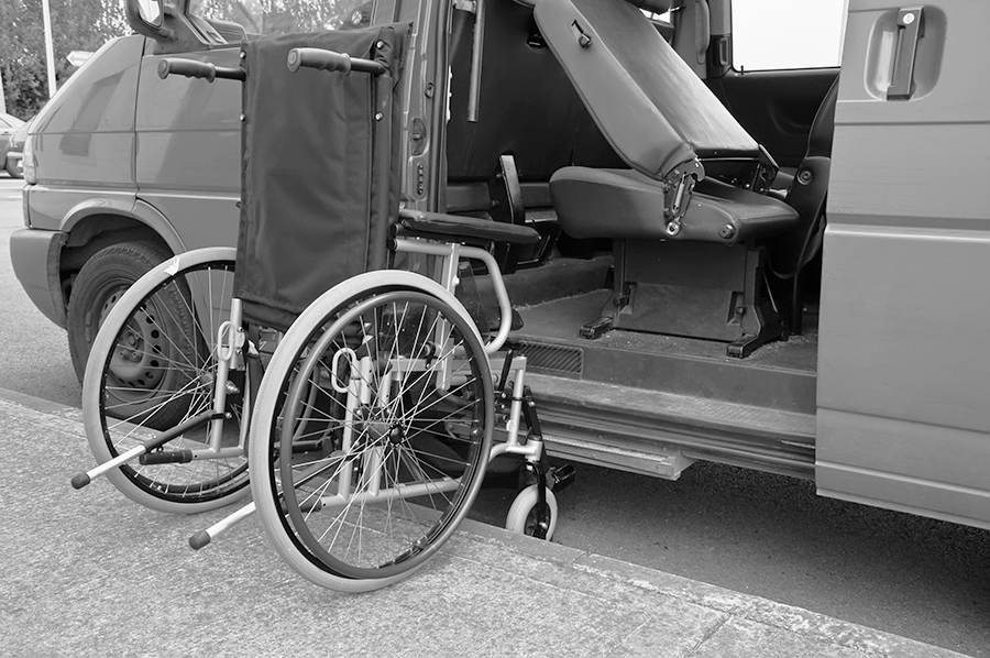 A wheelchair is positioned next to an accessible van equipped with a lift, showcasing mobility support for individuals with disabilities.