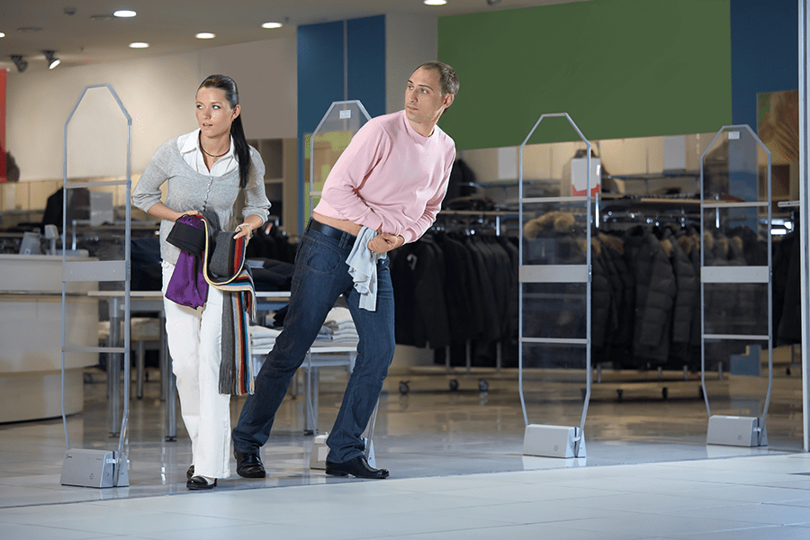 Two individuals appear to be sneaking out of a store, possibly shoplifting, with one looking back cautiously.