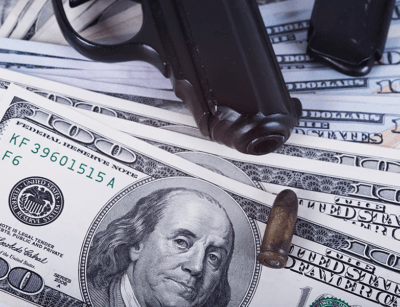 A handgun and bullets are lying on top of scattered US dollar bills.