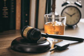 A gavel, car keys, and a glass of whiskey on a table suggesting the consequences of drinking and driving.