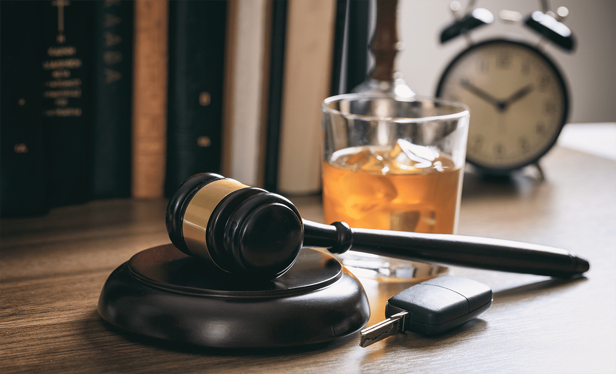 A gavel, car keys, and a glass of whiskey on a table suggesting the consequences of drinking and driving.