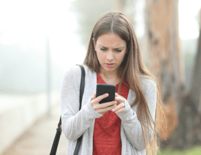 A woman appears concerned or confused while looking at her smartphone outdoors.