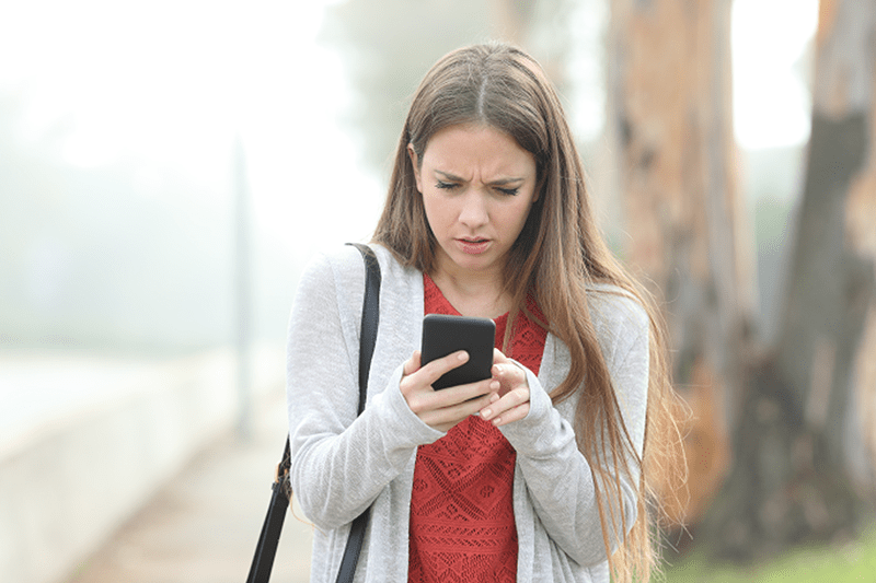 A woman appears concerned or confused while looking at her smartphone outdoors.