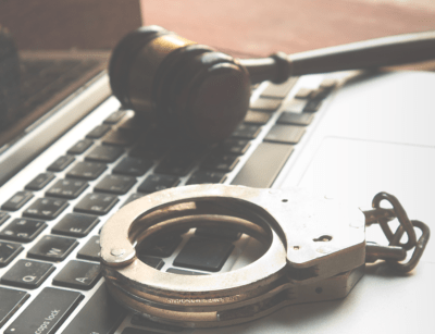 A gavel and handcuffs placed on a laptop keyboard, symbolizing law and cybersecurity.