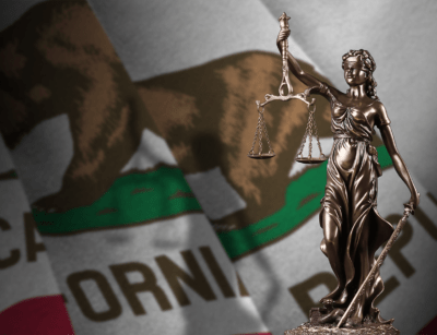 A statue of Lady Justice is in the foreground with the flag of California in the background.