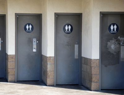 Three public restroom doors with gender symbols, two for men and one for women, with a slightly worn appearance.
